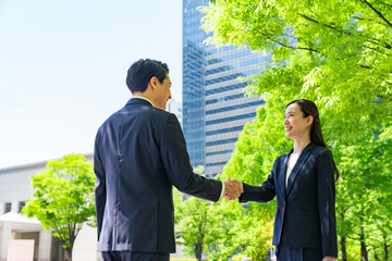 A group of business people shaking hands in a city with fresh greenery