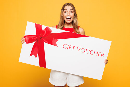 Young woman wear red casual clothes hold in hand paper package bags after shopping big gift coupon voucher card for store isolated on plain orange yellow background. Black Friday sale buy day concept.