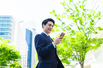 新緑の街でスマホを使う男性ビジネスパーソン