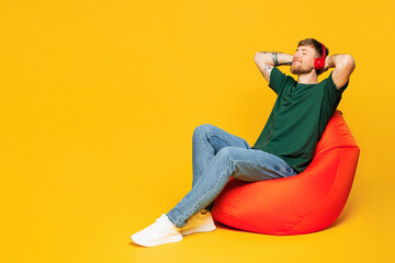 Full body young man he wear green t-shirt casual clothes sit in bag chair listen to calm music in...