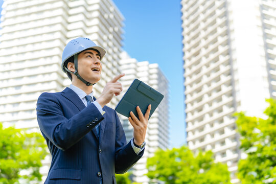 ビルの前でタブレットを使うヘルメットをかぶった男性ビジネスパーソン