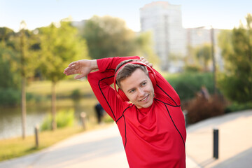Smiling sportsman in headphones doing morning exercise outdoors. Healthy lifestyle