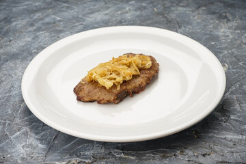fried steak with onions in a white plate on a gray concrete background