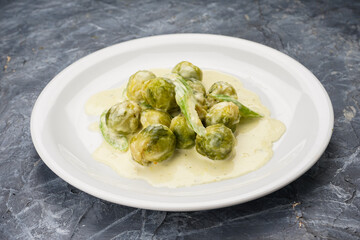 boiled Brussels sprouts with cream sauce in a white plate on a background
