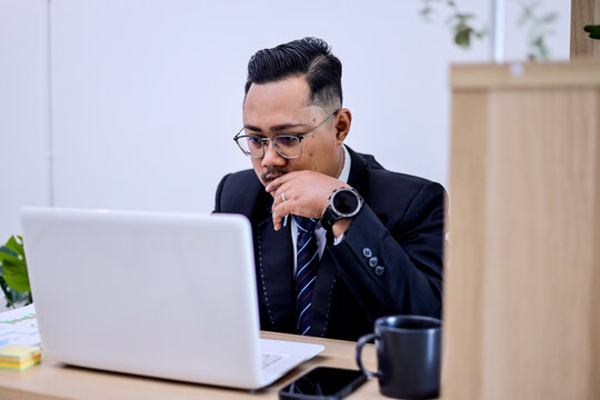 Thoughtful Businessman Focuses On Laptop Screen While Working In A Quiet Office Space