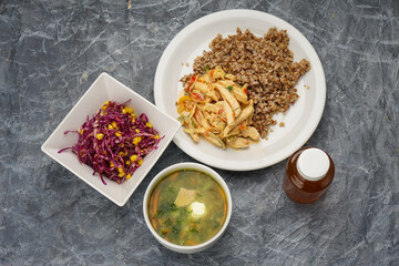buckwheat porridge with chicken and salad soup and compote on a gray background