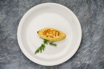 fried pie with herbs in a white plate on a gray background