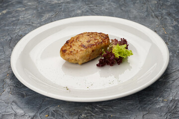 fried cutlet with herbs in a white plate on a gray background