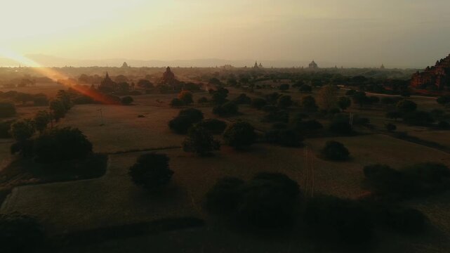 Aerial view of temples scattered amongst trees, the landscape bathed in the golden light of sunrise, creating a tranquil scene, Old Bagan, Mandalay Region, Myanmar.