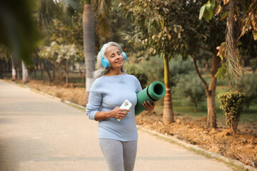 Beautiful Senior Woman Enjoying A Walk With Yoga Mat And Headphones