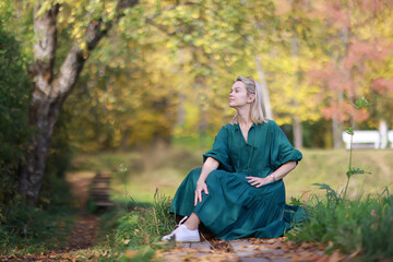 A woman in a long dress on the background of an autumn park is relaxing on a walk