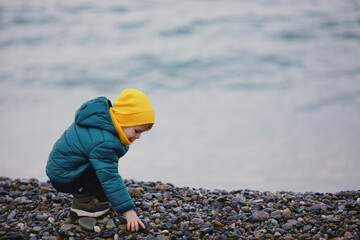 A 5-year-old boy in a warm jacket on the seashore during the cold off-season