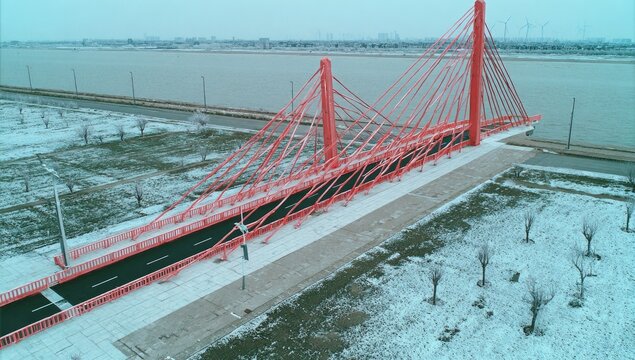 Red cable-stayed bridge over a river in winter