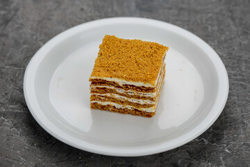 dessert honey cake with cream on a white plate on a gray background