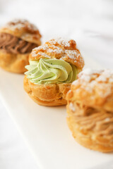 Three choux pastries with different fillings on white background