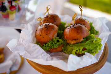 Gourmet sliders served on a wooden platter with fresh lettuce and special toppings at a casual outdoor gathering