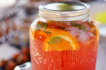 Refreshing summer drink with citrus and mint served in a glass jar at a sunny outdoor gathering