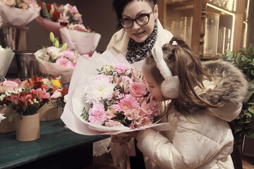 A girl and her grandmother choose and buy a bouquet of flowers at a flower shop, an autumn or...