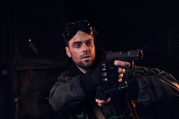 A young man stands ready with a firearm in a bleak, post apocalyptic environment defined by ruin.