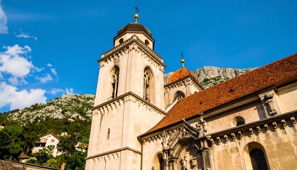 Fototapeta premium Stone church facade with a terracotta roof against a backdrop of mountains.