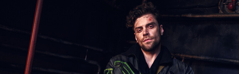 A young handsome man stands in a desolate environment, embodying strength amid chaos.