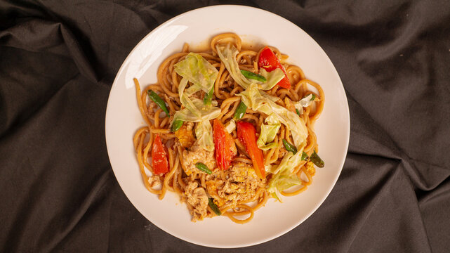 Mie Goreng Jawa or bakmi jawa or java noodle. Indonesian traditional street food noodles from central java or Yogyakarta, indonesia on black background. Flat lay photo. Isolated from dark background