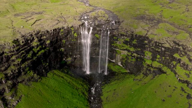 Aerial view of the cascading Foss&aacute; waterfall plunges down dark cliffs, contrasting with the vibrant green moss, Langasandur, Streymoy, Faroe Islands.