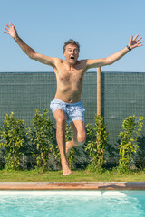 A man jumps with his arms outstretched to dive into the pool
