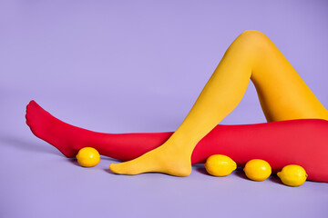 Long slim woman legs in multicolor yellow and red tights relax over purple studio background.
