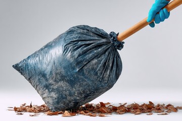 A hand in a blue glove pushes a filled trash bag over fallen leaves