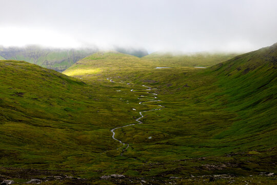 View of vibrant green slopes descend to meet a winding stream under a soft, clouded sky, creating a serene, natural vista, Tj&Atilde;&cedil;rnuv&Atilde;&shy;k, Streymoy, Faroe Islands.