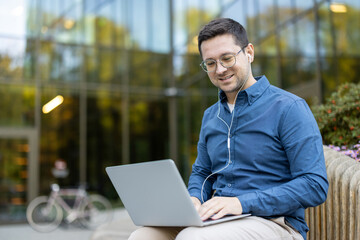 Man working on a laptop outdoors with earphones in a professional setting