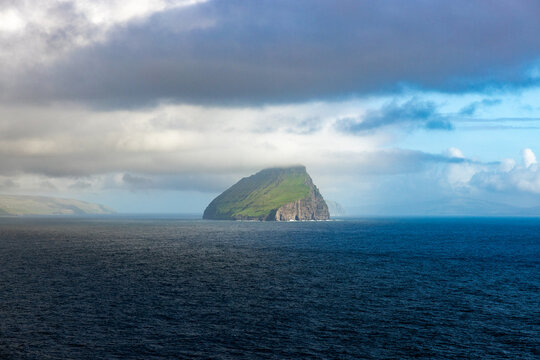 View of Tr&Atilde;&cedil;llkonufingur islet rising majestically from the deep blue sea under a cloudy sky, a rugged jewel of green and gray, Sandav&Atilde;&iexcl;gur, V&Atilde;&iexcl;gar, Faroe Islands.