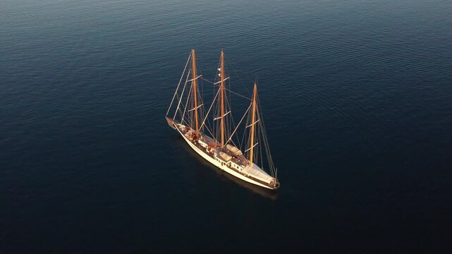 Ermioni, Greece - 29 July 2025: Aerial view of a white sailing boat cutting through the dark blue water, creating a stunning contrast of light and shadow.