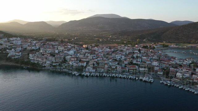 Ermioni, Greece - 29 July 2025: Aerial view of the townscape with white buildings and boats docked in the harbor, set against a backdrop of mountains.