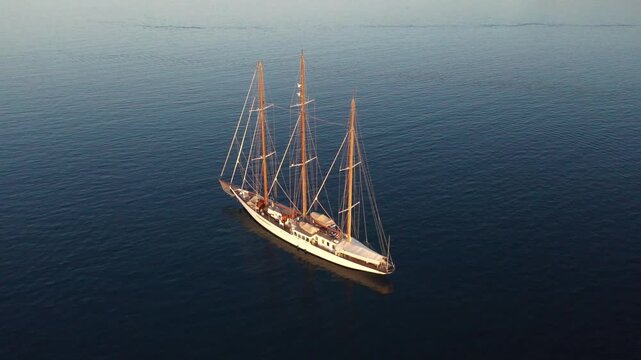 Ermioni, Greece - 29 July 2025: Aerial view of a sailing boat cutting through the dark blue waters, its white hull contrasting against the sea's surface.
