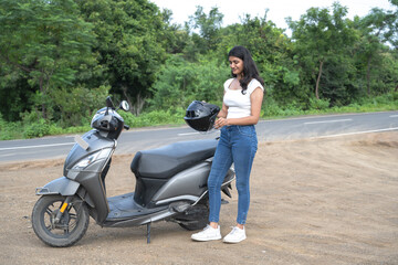 Strong independent Indian woman biker with her moped and helmet .