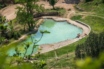 Bagno Vignoni, Tuscany, Italy - 28 April 2025: View of Bagno Vignoni's thermal waters, a tranquil oasis embraced by verdant hills, where sunlight dances on the aquamarine surface.