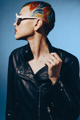 Young woman with colorful shaved hair and stylish sunglasses wearing a black leather jacket, posing...