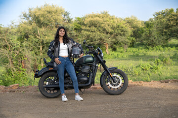 Strong independent Indian woman biker: beautiful girl, stylish rider, motorcycle adventure, elegant jacket, confident posture, powerful machine, free spirit, road journey, fearless attitude.