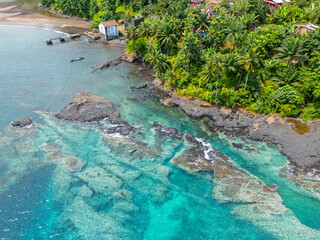 Aerial view of a coastal village in São Tomé with turquoise waters, volcanic rock formations, and...