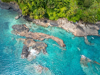 Aerial view of São Tomé’s tropical coastline near São João dos Angolares, with turquoise waters, black volcanic rocks, and dense palm forest.  
