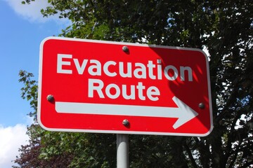 Fototapeta premium Red Evacuation Route Sign with Arrow Pointing Right under Tree Canopy.