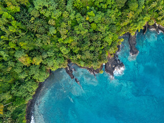 Aerial view of São Tomé’s tropical coastline near São João dos Angolares, with turquoise waters, black volcanic rocks, and dense palm forest.  
