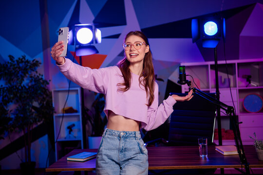 Popular female blogger live-streaming social media content in a trendy neon-lit studio with microphone and smartphone