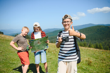 Children hiking in mountains using map and camera, enjoying summer vacation