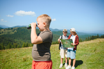 Children hiking in mountains using binoculars and map