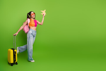 Young woman holding a travel toy plane with a suitcase on a vibrant green background exuding...