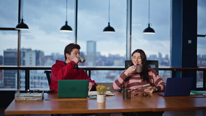Relaxed colleagues drinking coffee at open space. Two coworkers talking together