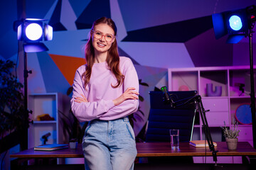 Professional female content creator working in a modern neon-lit office studio with a microphone...